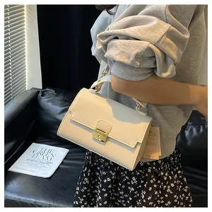 Detail of cream textured leather handbag with gold clasp held by a model in elegant setting