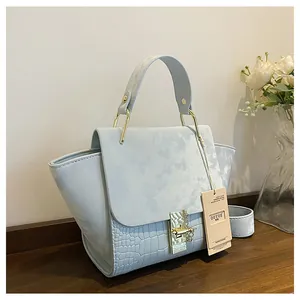 Detail of light blue handbag featuring crocodile texture and suede-like flap on wood table