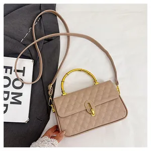 Dettaglio borsa trapuntata beige con manico in bambù dorato e chiusura in metallo a forma di U