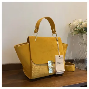 Detailed view of yellow trapezoid bag with crocodile texture and gold metal lock closure