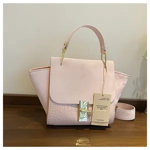 Detail of pink trapezoid bag featuring embossed crocodile pattern and gold hardware