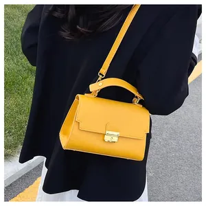 Minimalist yellow leather handbag with gold metal lock worn on a black blazer