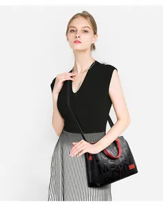 Detail of black leather handbag with red trim and embossed letters on a female model