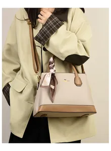 Close-up of contrast-colored leather handbag with gold kangaroo logo and decorative scarf