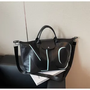 Detail of a large capacity black travel bag with light blue NO lettering and shoulder strap