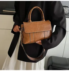 Dettaglio borsa marrone trama coccodrillo con elegante tracolla larga con scritte
