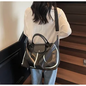 Detail view of a large black travel tote with bold white letters and leather top flap