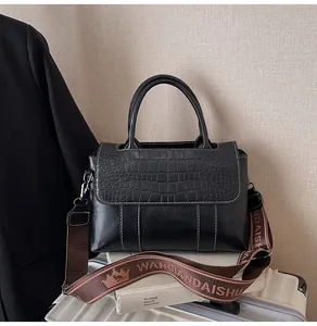 Dettaglio borsa nera con trama a coccodrillo, cuciture bianche e tracolla intrecciata