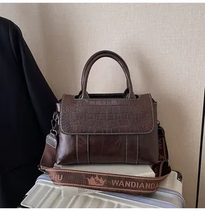 Dettaglio borsa marrone scuro con trama a coccodrillo e tracolla logo su valigia