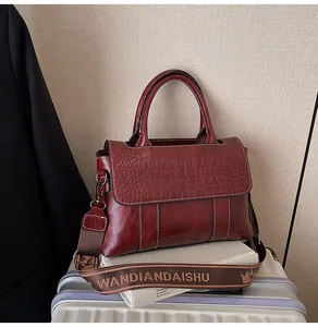 Dettaglio borsa coccodrillo bordeaux con tracolla larga logo su libri bianchi
