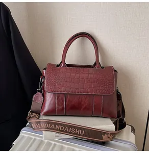 Dettaglio borsa a mano bordeaux effetto coccodrillo con tracolla in tessuto alla moda