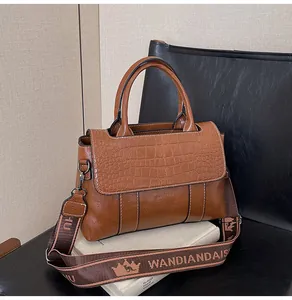 Dettaglio della patta con motivo coccodrillo su borsa in pelle marrone con tracolla
