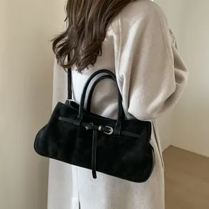 Sac baguette rétro en daim noir avec boucle porté sur un manteau en laine beige