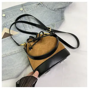 Gros plan du sac seau en daim marron avec surpiqûres matelassées sur veste en jean