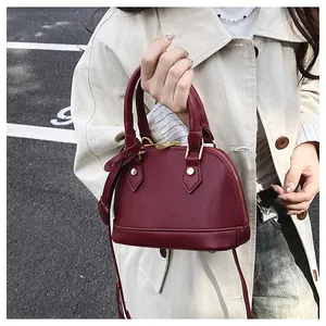 Dettaglio della trama bordeaux con motivo litchi e hardware dorato della borsa