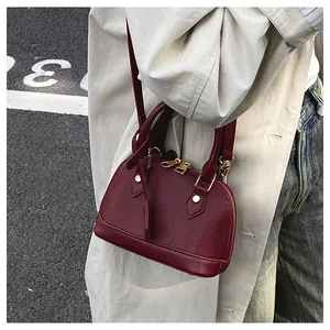 Elegante borsa a conchiglia in pelle bordeaux indossata a tracolla su outfit urban