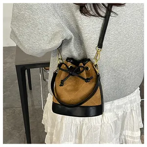 Détail du sac seau en daim marron avec surpiqûres matelassées et nœud de serrage élégant