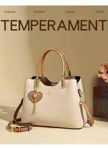 Detail of elegant two-tone tote bag with gold logo, heart pendant and leather straps
