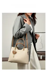 Detail of a beige leather handbag with brown handles and a heart charm on a model