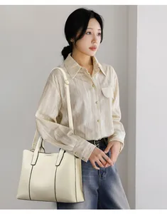 Grand sac cabas crème avec bordure noire et bandoulière porté par un mannequin en studio