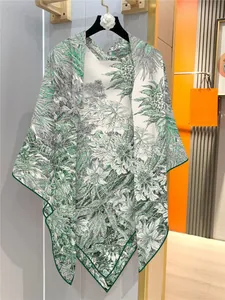 Detail of a white and green cashmere-feel scarf with tropical plant prints on a hanger