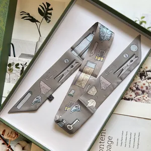 Détail d'un foulard en soie taupe à imprimé papeterie dans son coffret cadeau vert