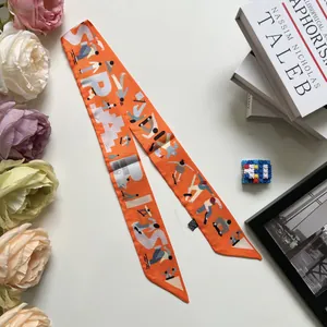 Détail d'un foulard en soie orange imprimé montrant des motifs d'art et des bords fins