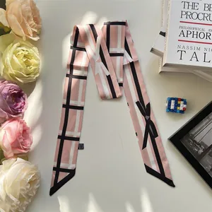 Pink silk-like twilly scarf with geometric bow pattern displayed on a desk