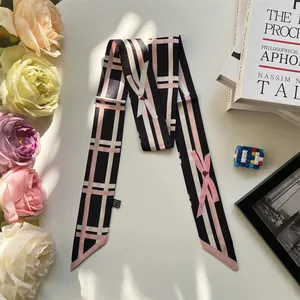 Detail of silk-like ribbon scarf featuring pink bows and plaid patterns on white background