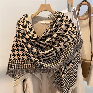 Detail of houndstooth scarf with fringe tassels worn over a beige wool coat