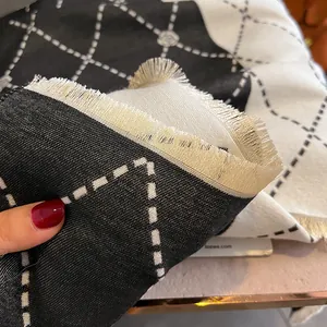 Close-up of black and white camellia pattern scarf with fringe edges and thick knit texture