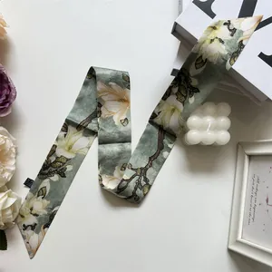 Gros plan d'un foulard en soie à fleurs de magnolia gris-vert avec étiquette cousue