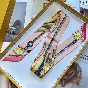 Detail of pink French silk scarf with chain print folded neatly inside a luxury yellow gift box