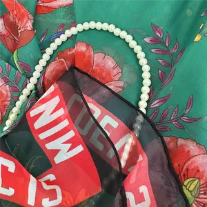 Dettaglio della trama in tessuto georgette con fiori rossi e collana di perle