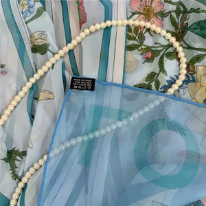 Dettaglio di sciarpa in seta floreale con etichetta di lavaggio e collana di perle eleganti