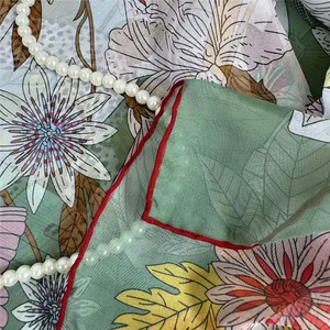 Detail van zijden sjaal met bloemenprint in lichtgroen met handgerolde rode randen