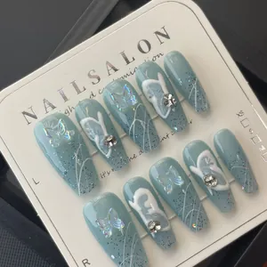 Detalle de uñas postizas azules con mariposas holográficas y pedrería en tarjeta
