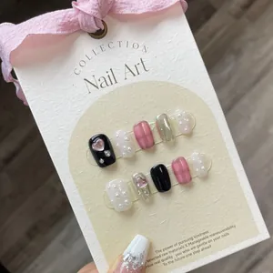 Pink and black checkered press-on nails set with heart and pearl accents on display