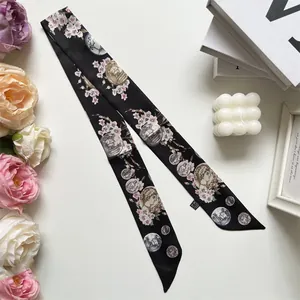 Close-up of narrow silk twilly scarf with pink floral and coin print on black background