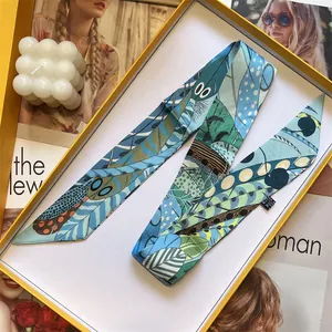 Detail view of tropical feather pattern narrow silk scarf inside a yellow gift box