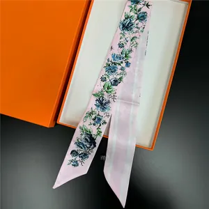 Detailed close-up of a pink satin twilly scarf with blue floral patterns in a gift box