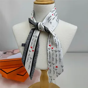 Detail of white silk scarf with 'Je vous adore' text and red hearts on a model