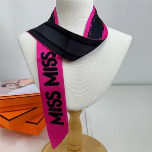 Gros plan d'un foulard en soie rose et noir avec imprimé MISS MISS noué au cou