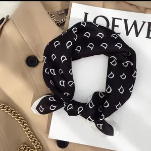 Close-up of elegant silk scarf with white D-pattern over black fabric and trench coat