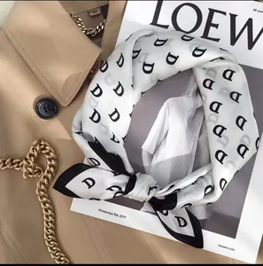 Detail of silk-feel scarf with black D-letter pattern paired with khaki trench coat