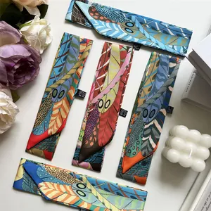 Detailed flat lay of assorted narrow twilly scarves with vibrant feather patterns on silk