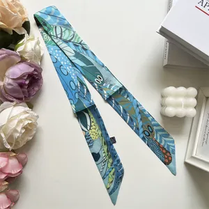 Detail of blue narrow silk scarf with feather patterns styled on white table background