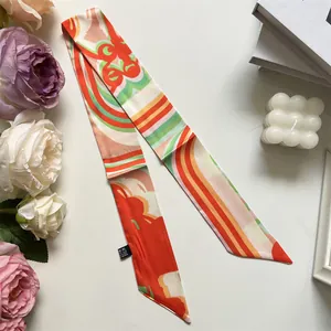 Detail of orange and green geometric silk-feel twilly scarf with care label and decor