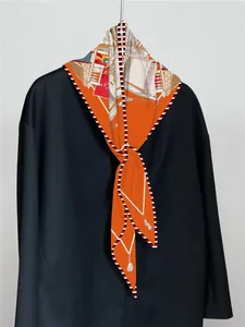 Nahaufnahme von orangem Seidenschal mit Kutschenmuster auf einem schwarzen Mantel