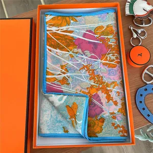 Detailed view of luxury silk scarf with floral patterns inside a vibrant orange gift box